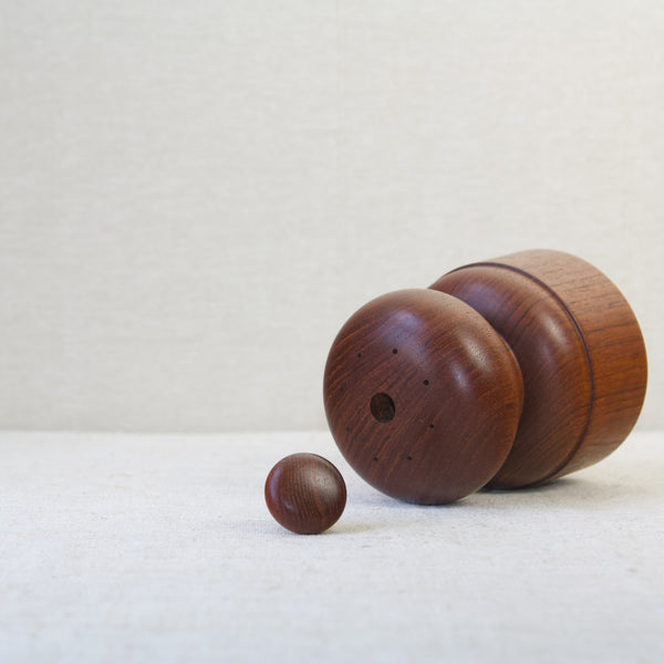 A carved solid teak salt and pepper mill designed by Jens Quistgaard for Dansk. The image shows the top of the domed mill where the eight holes for shaking salt are. The peg or stopper which plugs the refilling hole is removed from the mushroom and placed in the centre of the image. 