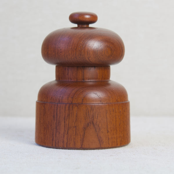 Head on close up of a teak wood "Mushroom" model 1616 pepper mill by Jens Quistgaard. This mill belongs to the mushroom family of shapes that are characterized by a round, columnal base, a slender neck, topped by a squashed ball resembling traditional convex cap fungi.