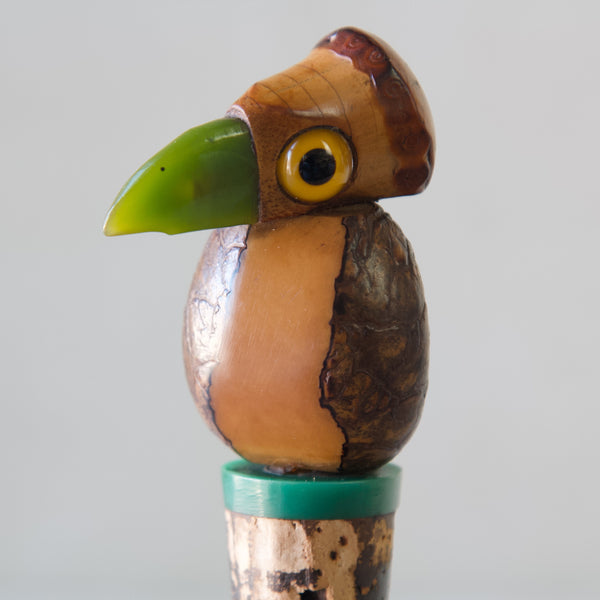 Detail shot of Henry Howell tagua nut bird bottle stopper with green bakelite beak and yellow glass eyes. 