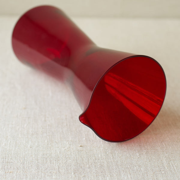 A vibrant ruby red cocktail pitcher by Kaj Franck, crafted in 1954, highlighting mid-century Scandinavian glass design.