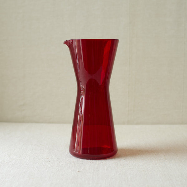 A vibrant ruby red cocktail pitcher designed by Kaj Franck in 1954, representing mid-century Scandinavian design.