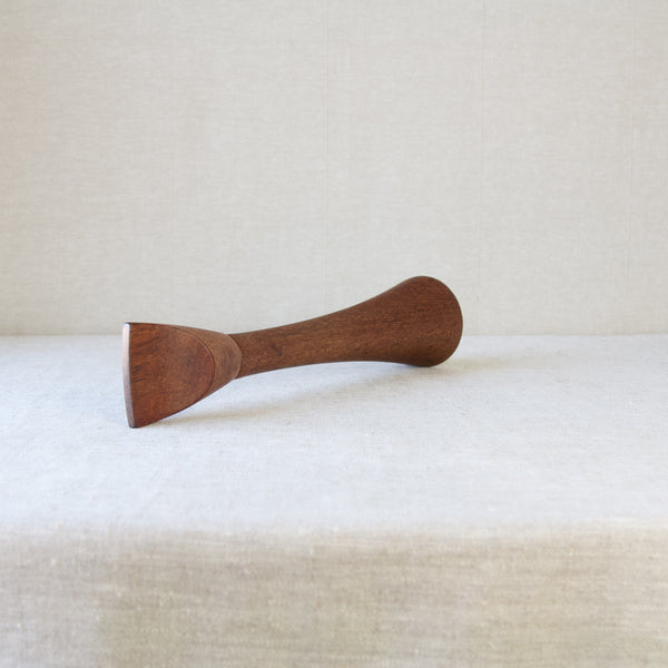 Head on shot of a tall slender teak wood pepper mill laying on its side. This organic modern design is a Scandinavian collectible by Jens Quistgaard. Many other examples of his work can be view at Art & Utility, an online London based Nordic design gallery.