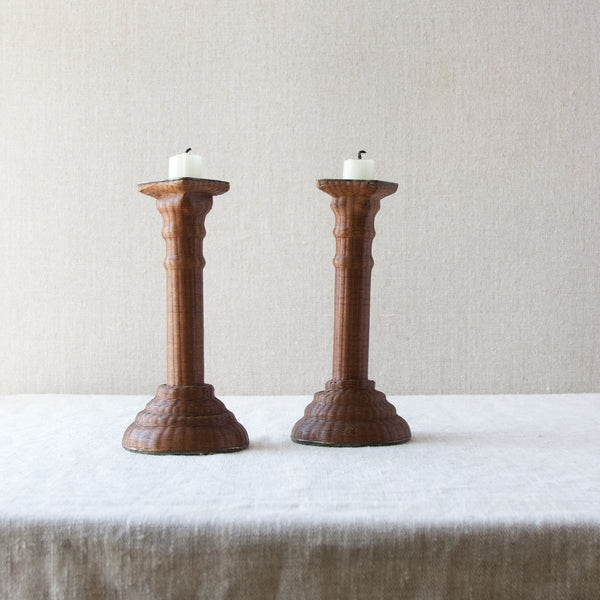 Mood image showing a pair of antique wickerwork candlesticks stood atop a linen table cloth. Chic antiques and design collectables available to view in South West London at Art & Utility.