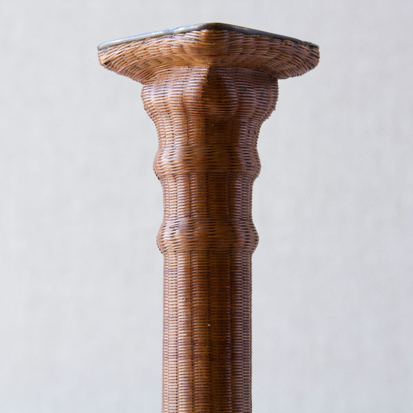 Close up of an 18th Century pewter candlestick formed into the shape of a neoclassical Doric column. Bizarrely but brilliantly, the entirety of the form has been wrapped in tiny woven cane rattan. 