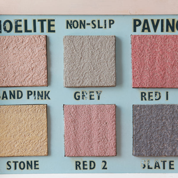 Detail of 6 colourful Noelite tiles mounted on a baby-blue coloured board, each square tile is named. Written are sand pink, grey, red 1, stone, red 2, and, slate.