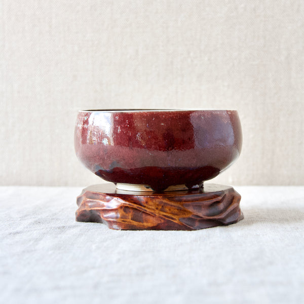 Mood image of a rare 1970s Swedish ox-blood glazed porcelain ceramic bowl hand-thrown by Carl-Harry Stalhane stood on top of an ancient Chinese wooden stand.