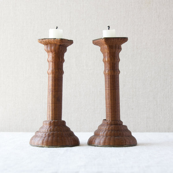 Large image of two historic antique candlesticks covered in woven wicker. The base or core of the form is pewter which has taken a few knocks over the years hence the somewhat wobbly appearance.