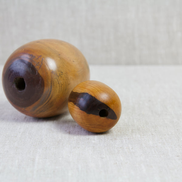Two lignum vitae plumber's bobbins laying on their sides. The holes drilled through them allows a rope to be attached. Once on a rope these hard ball objects were pulled through lead pipes to remove dents and kinks.