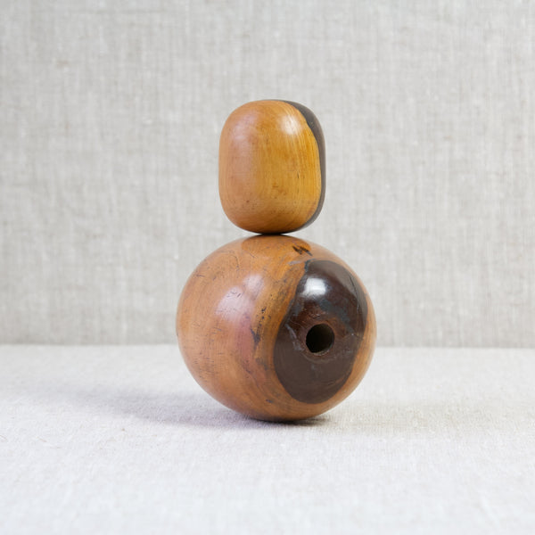A small lignum vitae bobbin stood atop a larger plumbers bobbin. Both are a golden honey colour with nut brown stripes.