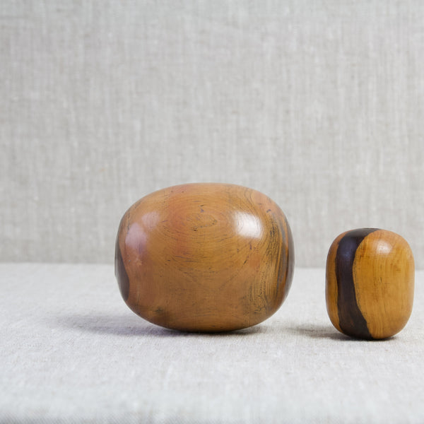 A large antique lignum vitae bobbin laying on its side next to a small plumber's bobbin. Both turned wooden objects boast a beautiful rich honey coloured patina.