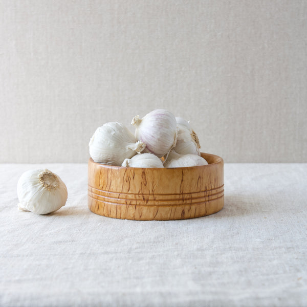 A Nordic handmade Karelian birch wood bowl filled with garlic bulbs.